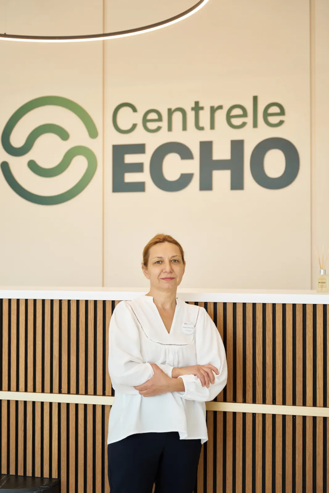 Angajată în uniformă albă stând cu brațele încrucișate în fața recepției Centrele ECHO, AsertivO Otopeni