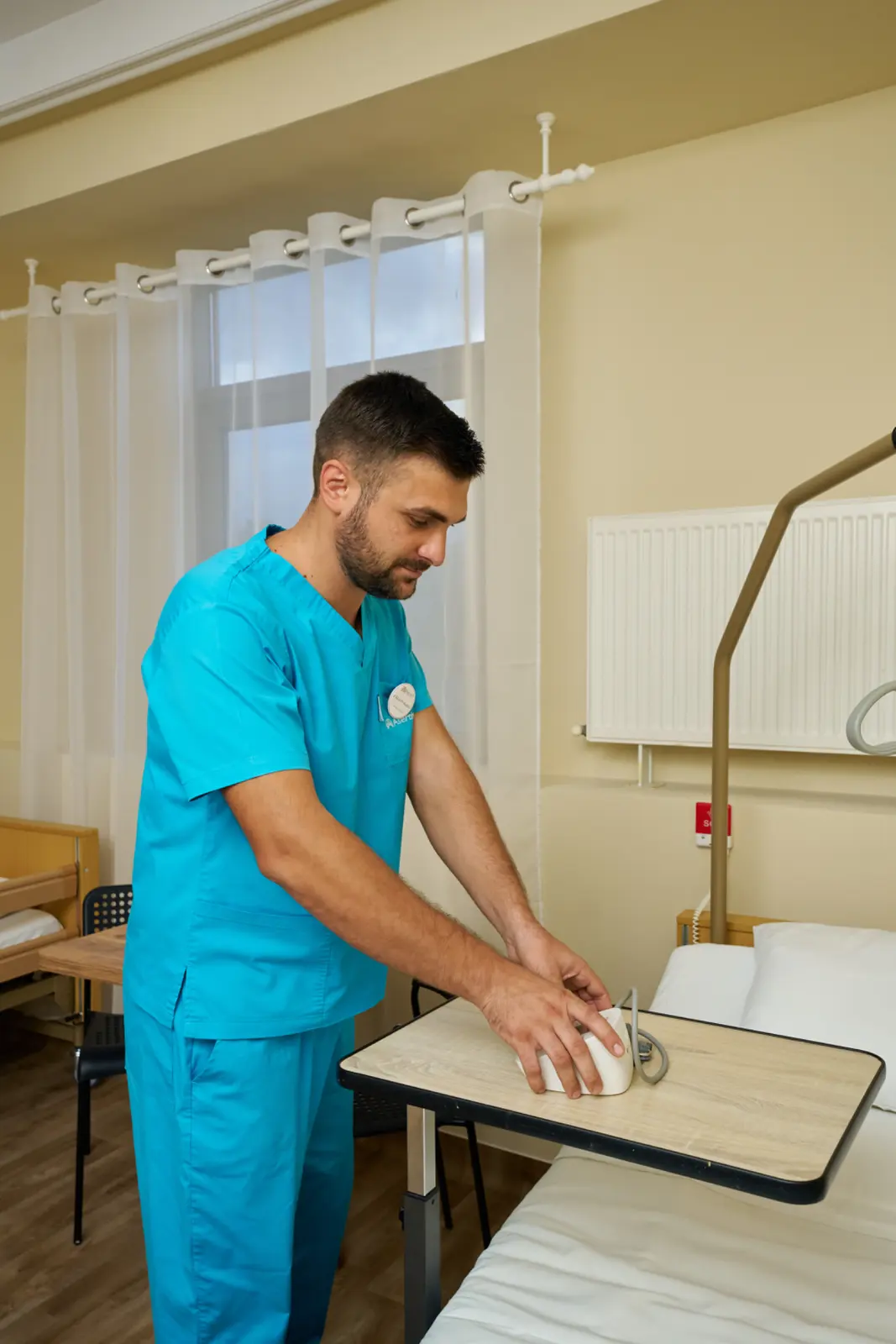 Asistent medical în scrubs turcoaz aranjează o cană albă pe masa rabatabilă dintr-o cameră, AsertivO Otopeni