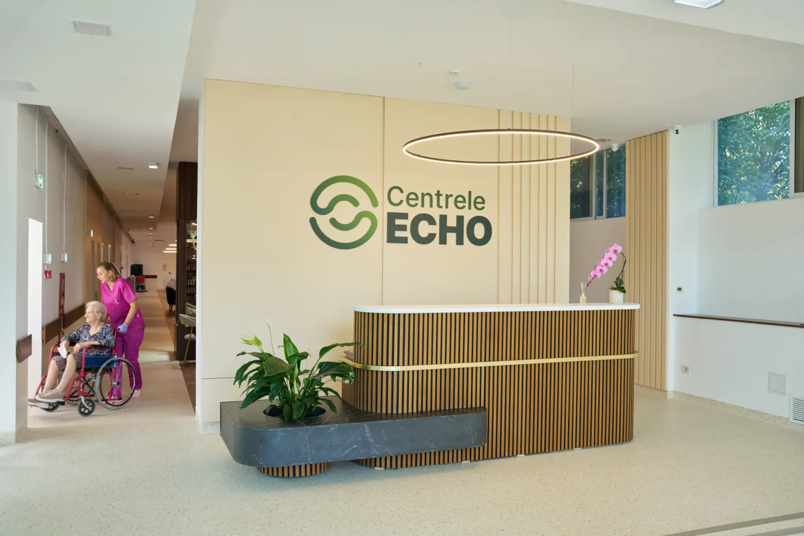 Recepție modernă a Centrelor Echo cu asistentă medicală în uniformă roz care însoțește o rezidentă, AsertivO Otopeni