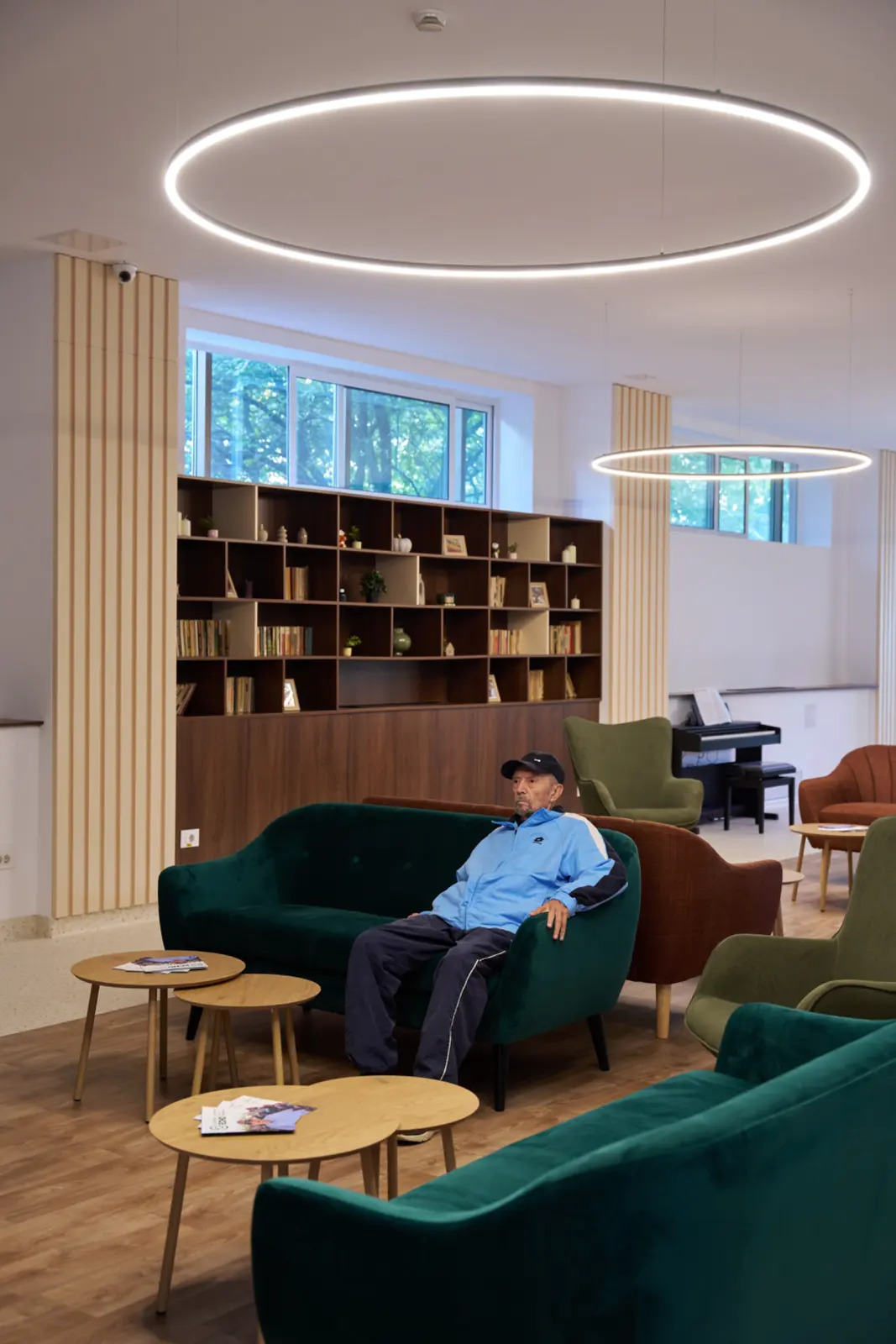 Senior în jachetă albastră așezat pe canapea verde de catifea într-o sală de relaxare modernă, AsertivO Otopeni